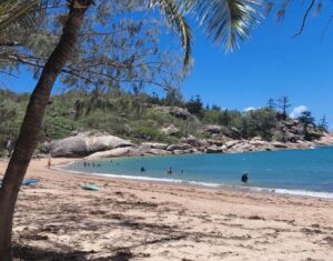 Pláž na Magnetic Island u Townsville, tyrkysové moře, palmy a skalnaté pobřeží v severním Queenslandu.