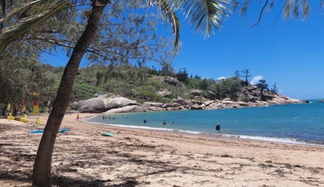 Pláž na Magnetic Island u Townsville, tyrkysové moře, palmy a skalnaté pobřeží v severním Queenslandu.